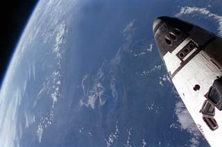 View of the space shuttle Atlantis, STS-71 mission, with a cloudy earth as a background. The payload bay is open as Atlantis makes preparations to dock with the Mir space station.